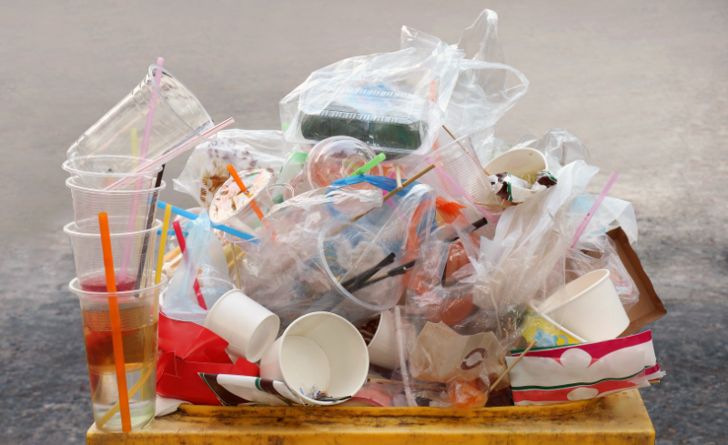 Contenedor desbordado con residuos plásticos y envases de un solo uso.